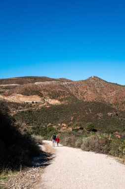 Yetişkinler, açık mavi gökyüzünün altında Akdeniz manzarasında yürüyüş yapıyor..