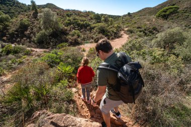 Baba ve kızı güneşli bir günde orman yolunda yürüyüş yapıyorlar..