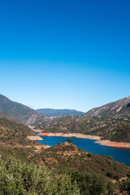 Bereketli yeşillik ve berrak mavi gökyüzünün altında dingin göl olan manzaralı dağ manzarası..