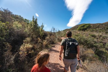 Genç yetişkinler bulutların oluşturduğu mavi gökyüzünün altında doğa yürüyüşü yapıyorlar..