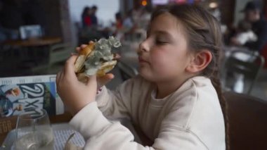 Genç kız hareketli bir restoranda hamburgerin tadını çıkarıyor..