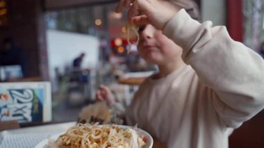 Genç kız kalabalık bir kafeteryada lezzetli bir yemeğin tadını çıkarıyor..