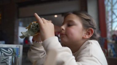 Meşgul bir kafede lezzetli bir burgerin tadını çıkaran genç bir kız..