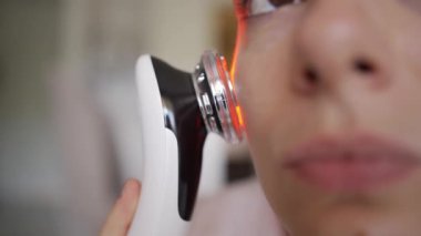Kadın, yüz hatları ve cilt bakımı için EMS kaldırma ve LED ışık terapi cihazı kullanıyor. Yüksek kalite 4k görüntü