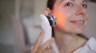 Kadın, yüz hatları ve cilt bakımı için EMS kaldırma ve LED ışık terapi cihazı kullanıyor. Yüksek kalite 4k görüntü