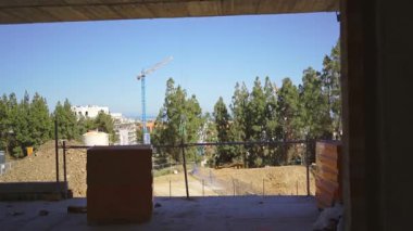 Ağaçların manzarası ve açık mavi gökyüzünün altında uzak bir vinç olan manzaralı kentsel inşaat alanı. Yüksek kalite 4k görüntü