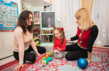 Anne ve kız arkadaşı yerde kızıyla oyuncak bebeklerle oynuyorlar.