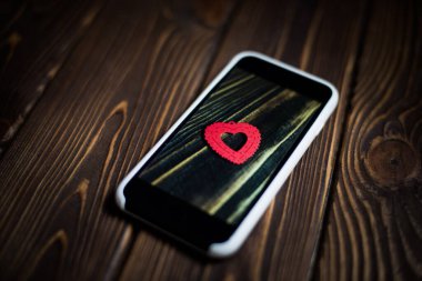 Ahşap arka planda akıllı telefon ve ekranda bir kalp sembolü