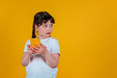 Neşeli, sevimli, kıvırcık bir kızın, parlak bir arka planda izole bir şekilde elinde telefon tutarken çekilmiş fotosu.