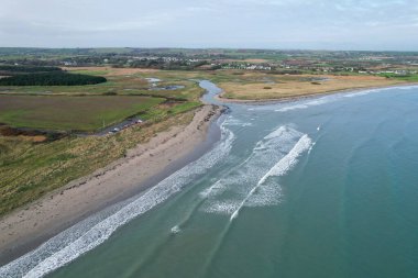 İrlanda 'daki Ballynamona Strand Sahili' nin geniş kumlu kıyı şeridini, yumuşak dalgaları ve yukarıdan yemyeşil kıyı çevresini gösteren geniş bir hava manzarası..