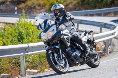 Motosiklet sürücüsü, arka planı doğa ve mavi gökyüzü olan ön planda bir viraj alıyor.