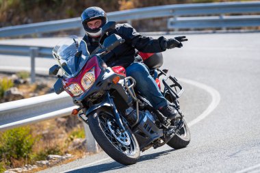 Motosiklet sürücüsü, arka planı doğa ve mavi gökyüzü olan ön planda bir viraj alıyor.