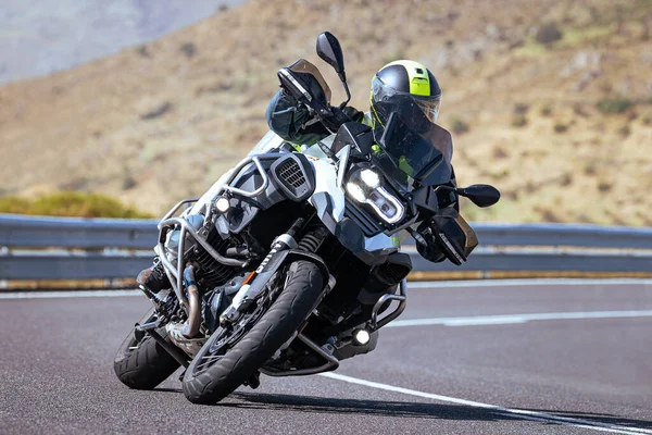 Motosiklet sürücüsü, arka planı doğa ve mavi gökyüzü olan ön planda bir viraj alıyor.