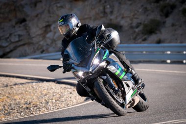 Aracındaki motosikletçi dağ yolunda viraj alıyor ve güneşli bir gün ve mavi gökyüzü var. Fotoğraf 16 Eylül 2022 'de İspanya' nın Avila ilindeki Navalmoral limanında çekildi.