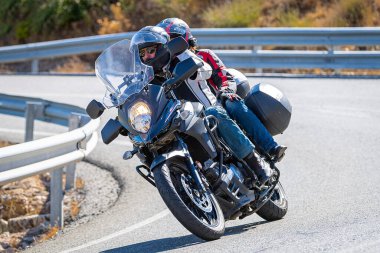 Aracındaki motosikletçi dağ yolunda viraj alıyor ve güneşli bir gün ve mavi gökyüzü var. Fotoğraf 16 Eylül 2022 'de İspanya' nın Avila ilindeki Navalmoral limanında çekildi.