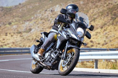 Aracındaki motosikletçi dağ yolunda viraj alıyor ve güneşli bir gün ve mavi gökyüzü var. Fotoğraf 16 Eylül 2022 'de İspanya' nın Avila ilindeki Navalmoral limanında çekildi.