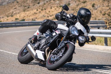 Aracındaki motosikletçi dağ yolunda viraj alıyor ve güneşli bir gün ve mavi gökyüzü var. Fotoğraf 20 Ağustos 2020 'de İspanya' nın Avila ilindeki Navalmoral limanında çekildi.