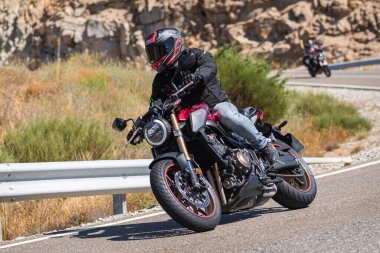 Aracındaki motosikletçi dağ yolunda viraj alıyor ve güneşli bir gün ve mavi gökyüzü var. Fotoğraf 20 Ağustos 2020 'de İspanya' nın Avila ilindeki Navalmoral limanında çekildi.