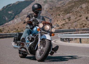 Aracındaki motosikletçi dağ yolunda viraj alıyor ve güneşli bir gün ve mavi gökyüzü var. Fotoğraf 20 Ağustos 2020 'de İspanya' nın Avila ilindeki Navalmoral limanında çekildi.