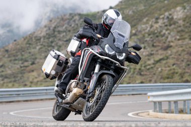 Motorsikletinde oturan bir adam, dağ yolunda keskin bir dönüş yapıyor. Fotoğraf Ağustos 2020 'de Avila şehrinde çekildi.