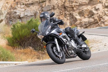 Motorsikletinde oturan bir adam, dağ yolunda keskin bir dönüş yapıyor. Fotoğraf Ağustos 2020 'de Avila şehrinde çekildi.