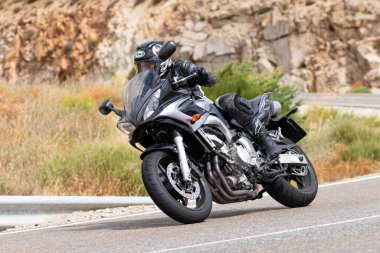 Motorsikletinde oturan bir adam, dağ yolunda keskin bir dönüş yapıyor. Fotoğraf Ağustos 2020 'de Avila şehrinde çekildi.