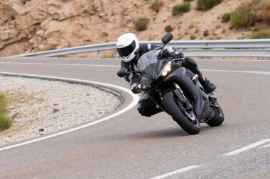 Motorsikletinde oturan bir adam, dağ yolunda keskin bir dönüş yapıyor. Fotoğraf Ağustos 2020 'de Avila şehrinde çekildi.