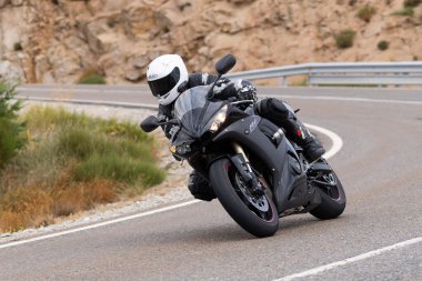 Motorsikletinde oturan bir adam, dağ yolunda keskin bir dönüş yapıyor. Fotoğraf Ağustos 2020 'de Avila şehrinde çekildi.