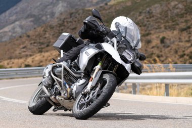 Motorsikletinde oturan bir adam, dağ yolunda keskin bir dönüş yapıyor. Fotoğraf Ağustos 2020 'de Avila şehrinde çekildi.