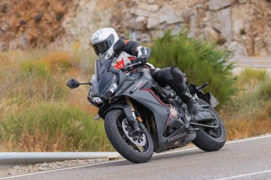 Yoldaki virajda motosikletini süren genç bir adam, ön planda güneşli bir günde fotoğraf. Fotoğraf Ağustos 2021 'de İspanya' nın Avila ilinde çekildi.