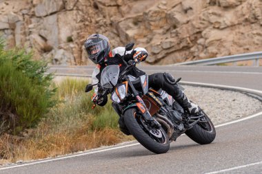 Yoldaki virajda motosikletini süren genç bir adam, ön planda güneşli bir günde fotoğraf. Fotoğraf Ağustos 2021 'de İspanya' nın Avila ilinde çekildi.