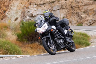 Yoldaki virajda motosikletini süren genç bir adam, ön planda güneşli bir günde fotoğraf. Fotoğraf Ağustos 2021 'de İspanya' nın Avila ilinde çekildi.