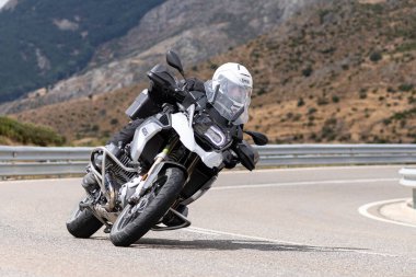 Yoldaki virajda motosikletini süren genç bir adam, ön planda güneşli bir günde fotoğraf. Fotoğraf Ağustos 2021 'de İspanya' nın Avila ilinde çekildi.