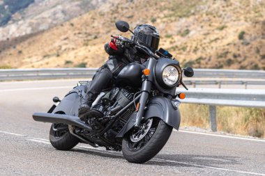 Yoldaki virajda motosikletini süren genç bir adam, ön planda güneşli bir günde fotoğraf. Fotoğraf Ağustos 2021 'de İspanya' nın Avila ilinde çekildi.