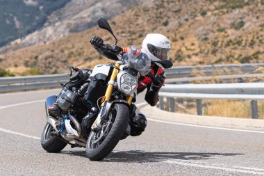 Yoldaki virajda motosikletini süren genç bir adam, ön planda güneşli bir günde fotoğraf. Fotoğraf Ağustos 2021 'de İspanya' nın Avila ilinde çekildi.