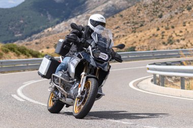 Yoldaki virajda motosikletini süren genç bir adam, ön planda güneşli bir günde fotoğraf. Fotoğraf Ağustos 2021 'de İspanya' nın Avila ilinde çekildi.