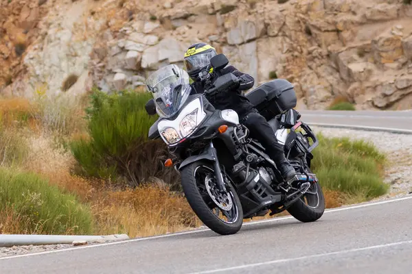 Yoldaki virajda motosikletini süren genç bir adam, ön planda güneşli bir günde fotoğraf. Fotoğraf Ağustos 2021 'de İspanya' nın Avila ilinde çekildi.