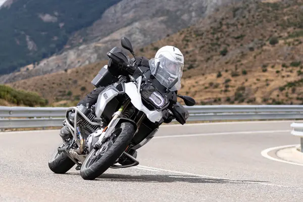 Yoldaki virajda motosikletini süren genç bir adam, ön planda güneşli bir günde fotoğraf. Fotoğraf Ağustos 2021 'de İspanya' nın Avila ilinde çekildi.