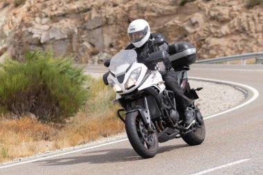 Motorsikletinin üstünde oturan, limanda yüksek hızda gezen ve güneşli bir günde viraj alan bir adam. Fotoğraf Temmuz 2020 'de İspanya' nın Avila kentindeki Navalmoral de la Sierra kasabasında çekildi.