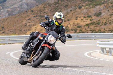 Motorsikletinin üstünde oturan, limanda yüksek hızda gezen ve güneşli bir günde viraj alan bir adam. Fotoğraf Temmuz 2020 'de İspanya' nın Avila kentindeki Navalmoral de la Sierra kasabasında çekildi.