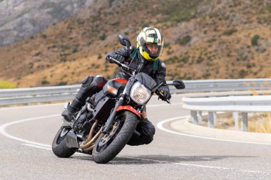 Motorsikletinin üstünde oturan, limanda yüksek hızda gezen ve güneşli bir günde viraj alan bir adam. Fotoğraf Temmuz 2020 'de İspanya' nın Avila kentindeki Navalmoral de la Sierra kasabasında çekildi.