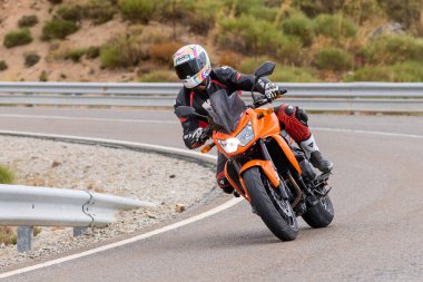 Motorsikletinin üstünde oturan, limanda yüksek hızda gezen ve güneşli bir günde viraj alan bir adam. Fotoğraf Temmuz 2020 'de İspanya' nın Avila kentindeki Navalmoral de la Sierra kasabasında çekildi.