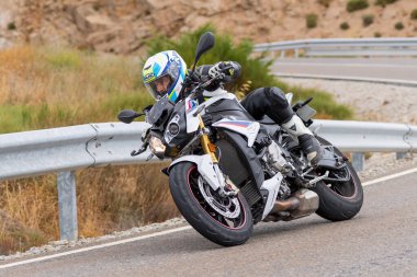 Motorsikletinin üstünde oturan, limanda yüksek hızda gezen ve güneşli bir günde viraj alan bir adam. Fotoğraf Temmuz 2020 'de İspanya' nın Avila kentindeki Navalmoral de la Sierra kasabasında çekildi.