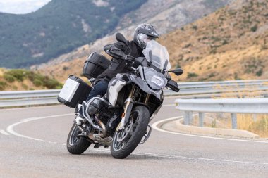 Motorsikletinin üstünde oturan, limanda yüksek hızda gezen ve güneşli bir günde viraj alan bir adam. Fotoğraf Temmuz 2020 'de İspanya' nın Avila kentindeki Navalmoral de la Sierra kasabasında çekildi.