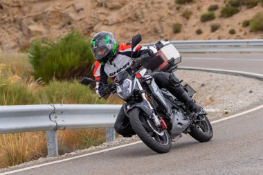 Motorsikletinin üstünde oturan, limanda yüksek hızda gezen ve güneşli bir günde viraj alan bir adam. Fotoğraf Temmuz 2020 'de İspanya' nın Avila kentindeki Navalmoral de la Sierra kasabasında çekildi.