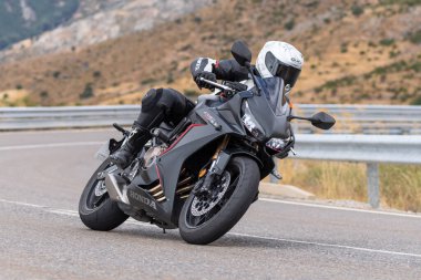 Motorsikletinin üstünde oturan, limanda yüksek hızda gezen ve güneşli bir günde viraj alan bir adam. Fotoğraf Temmuz 2020 'de İspanya' nın Avila kentindeki Navalmoral de la Sierra kasabasında çekildi.