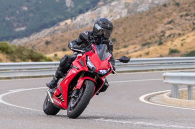 Motorsikletinin üstünde oturan, limanda yüksek hızda gezen ve güneşli bir günde viraj alan bir adam. Fotoğraf Temmuz 2020 'de İspanya' nın Avila kentindeki Navalmoral de la Sierra kasabasında çekildi.