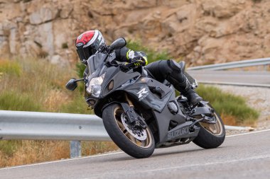 Motorsikletinin üstünde oturan, limanda yüksek hızda gezen ve güneşli bir günde viraj alan bir adam. Fotoğraf Temmuz 2020 'de İspanya' nın Avila kentindeki Navalmoral de la Sierra kasabasında çekildi.