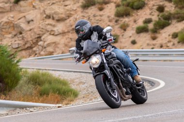 Motorsikletinin üstünde oturan, limanda yüksek hızda gezen ve güneşli bir günde viraj alan bir adam. Fotoğraf Temmuz 2020 'de İspanya' nın Avila kentindeki Navalmoral de la Sierra kasabasında çekildi.