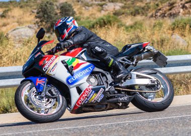 Yoldaki virajda motosikletini süren genç bir adam, ön planda güneşli bir günde fotoğraf. Fotoğraf Ağustos 2021 'de İspanya' nın Avila ilinde çekildi.